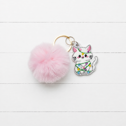 Christmas Light Kitten Pom Pom Keychain on clean white painted wood background