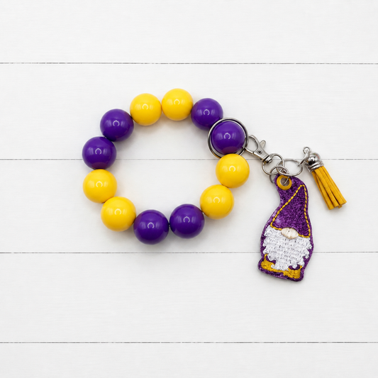 Purple and Gold Gnome Keychain with Beaded Wristlet on clean white wood background