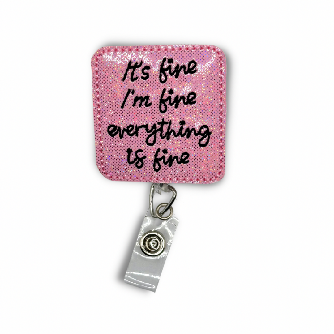 A felt badge reel with a pink background and black text that reads "It’s fine, I'm fine, Everything is fine". The badge reel features a clip on the back and a clear vinyl strap to hold an ID or badge.
