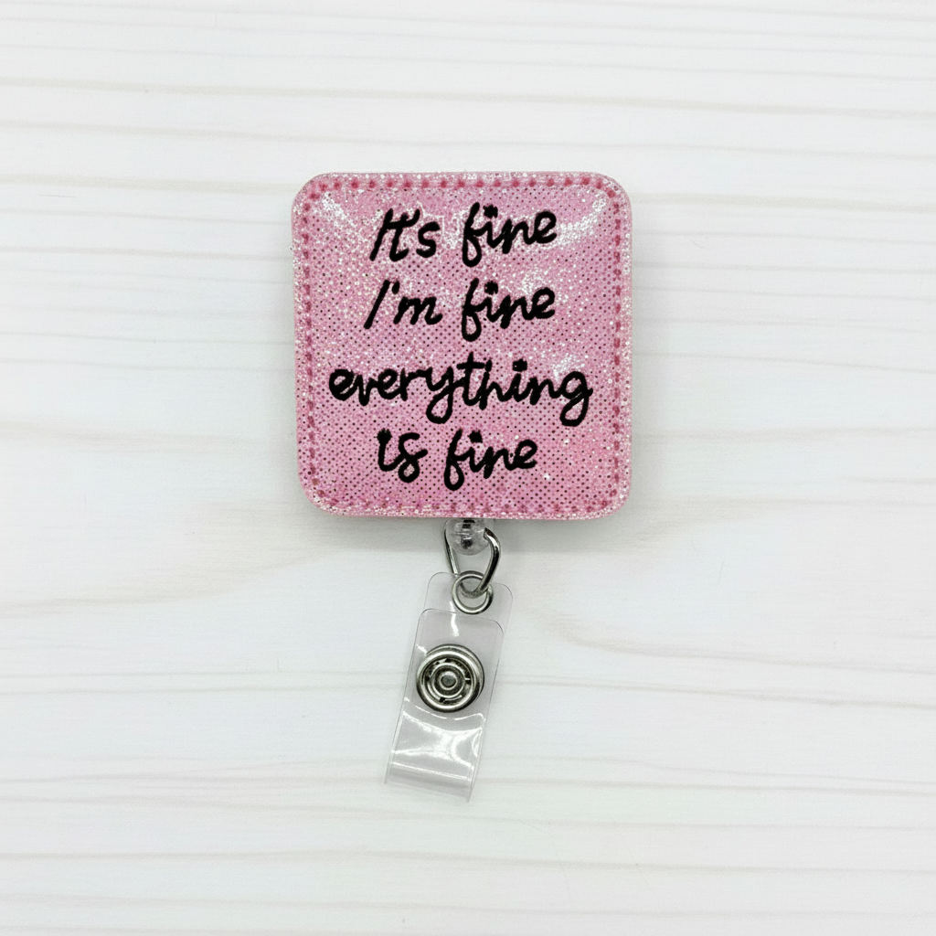 A felt badge reel with a pink background and black text that reads "It’s fine, I'm fine, Everything is fine". The badge reel features a clip on the back and a clear vinyl strap to hold an ID or badge.