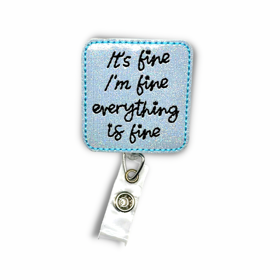 A felt badge reel with a blue background and black text that reads "It’s fine, I'm fine, Everything is fine". The badge reel features a clip on the back and a clear vinyl strap to hold an ID or badge.